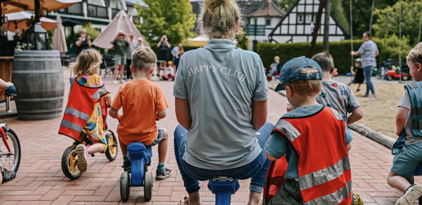 Kinder spielen draußen mit einer Mitarbeiterin des Happy Clubs