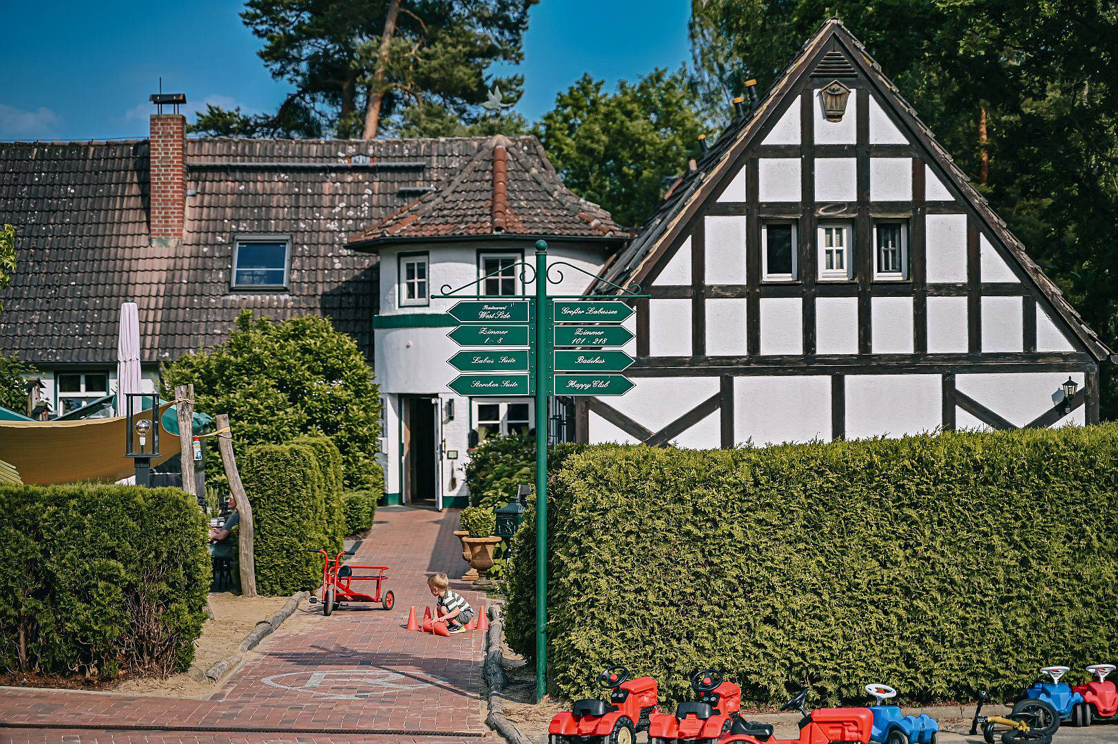 Haupthaus des Borchards Rookhus im Fachwerk Stil, mit Wegschildern und ein Kind spielt mit Hütchen am Boden