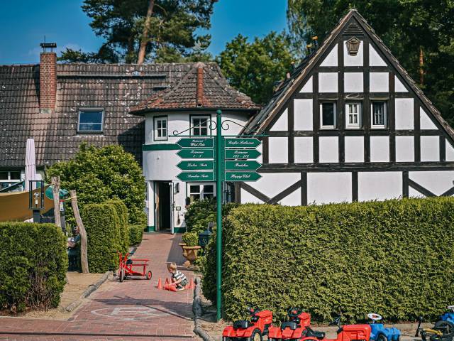 Haupthaus des Borchards Rookhus im Fachwerk Stil, mit Wegschildern und ein Kind spielt mit Hütchen am Boden