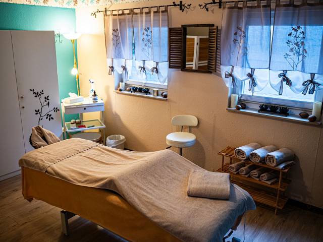 Wellnessraum, in dem es eine Massageliege gibt, verschiedene Wellnessutensilien und Handtücher