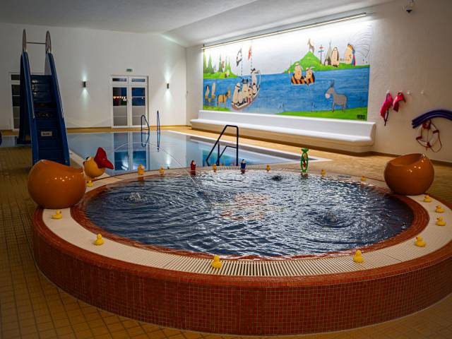 Aufnahme des Babybeckens mit Quietschenten am Poolrand, großem Pool, Wasserrutsche und großem Bild an der Wand