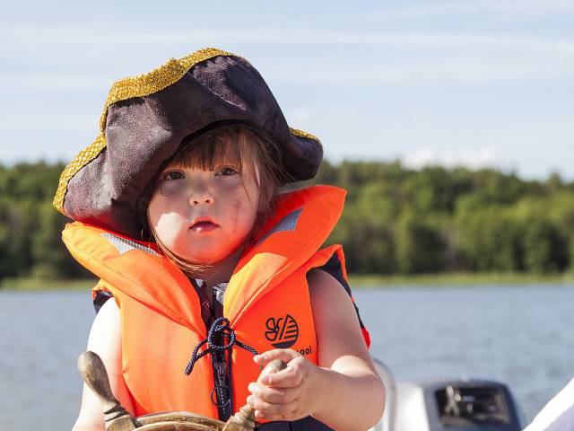 Kleiner Junge mit Schwimmweste, Piratenhut und Steuer in den Händen auf dem Labussee