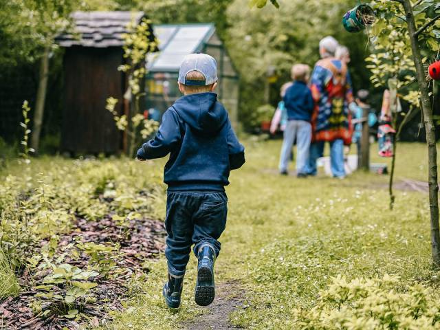 kleiner Junge läuft im Garten mit Gummistiefeln zu Familie