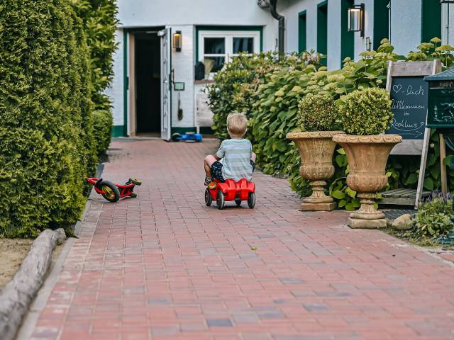 Kleiner Junge fährt mit Bobbycar am Hotel entlang