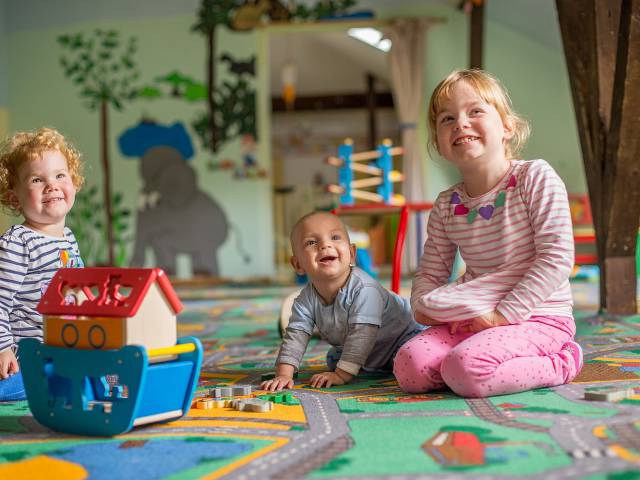 Drei Kinder spielen auf Spielteppich und lachen