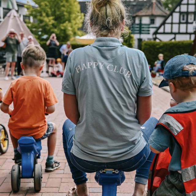 Kinder spielen draußen mit einer Mitarbeiterin des Happy Clubs