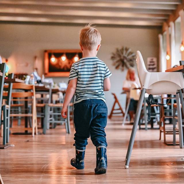 Kleiner Junge mit Gummistiefel läuft durch das Restaurant