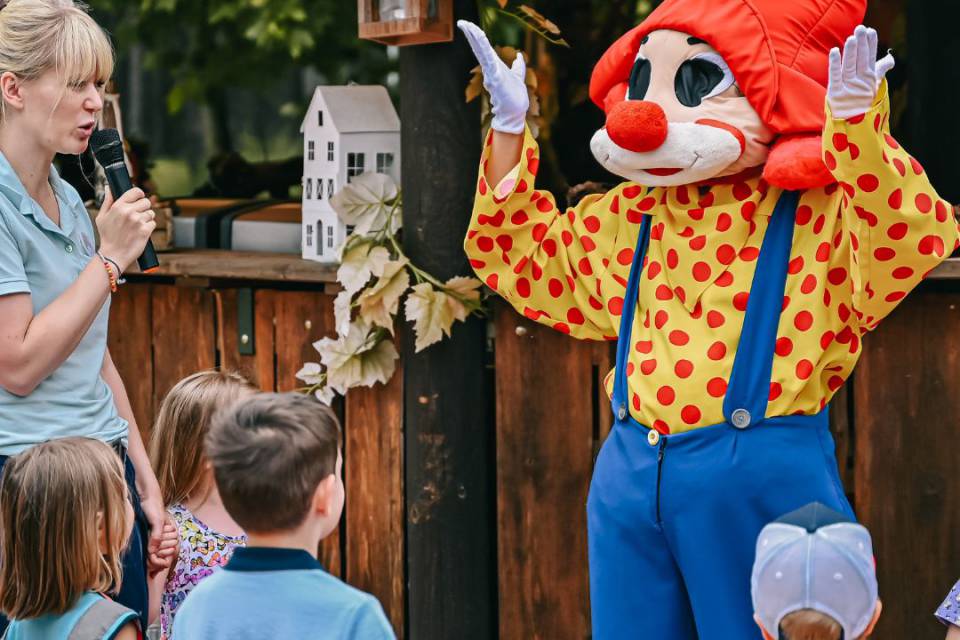 Kinder schauen Maskottchen Happy an und eine Betreuerin moderiert