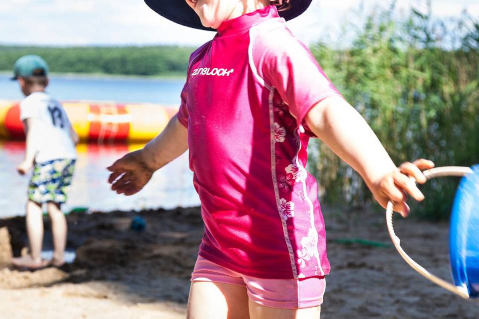 Kleines Mädchen mit Hut und Badekleidung läuft lachend im Sand