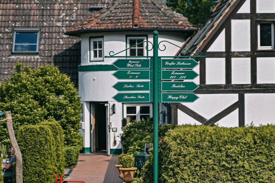 Borchards Rookhus Fachwerkhaus von außen, mit Wegschildern und ein Junge spielt mit Hütchen