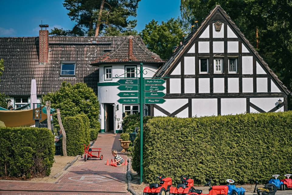 Haupthaus des Borchards Rookhus im Fachwerk Stil, mit Wegschildern und ein Kind spielt mit Hütchen am Boden