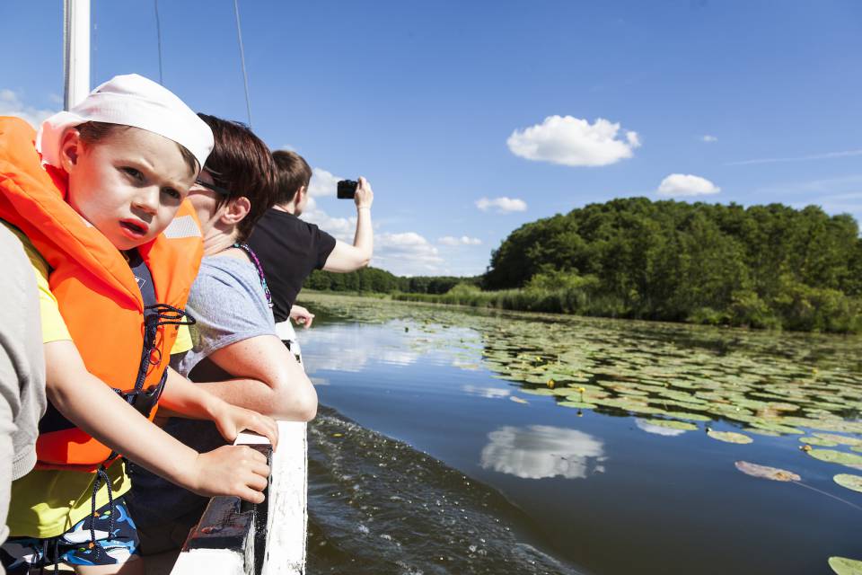 Eine Familie fährt mit dem Boot über die mecklenburgische Seenplatte. Man sieht blauen Himmel und viele Seerosen.