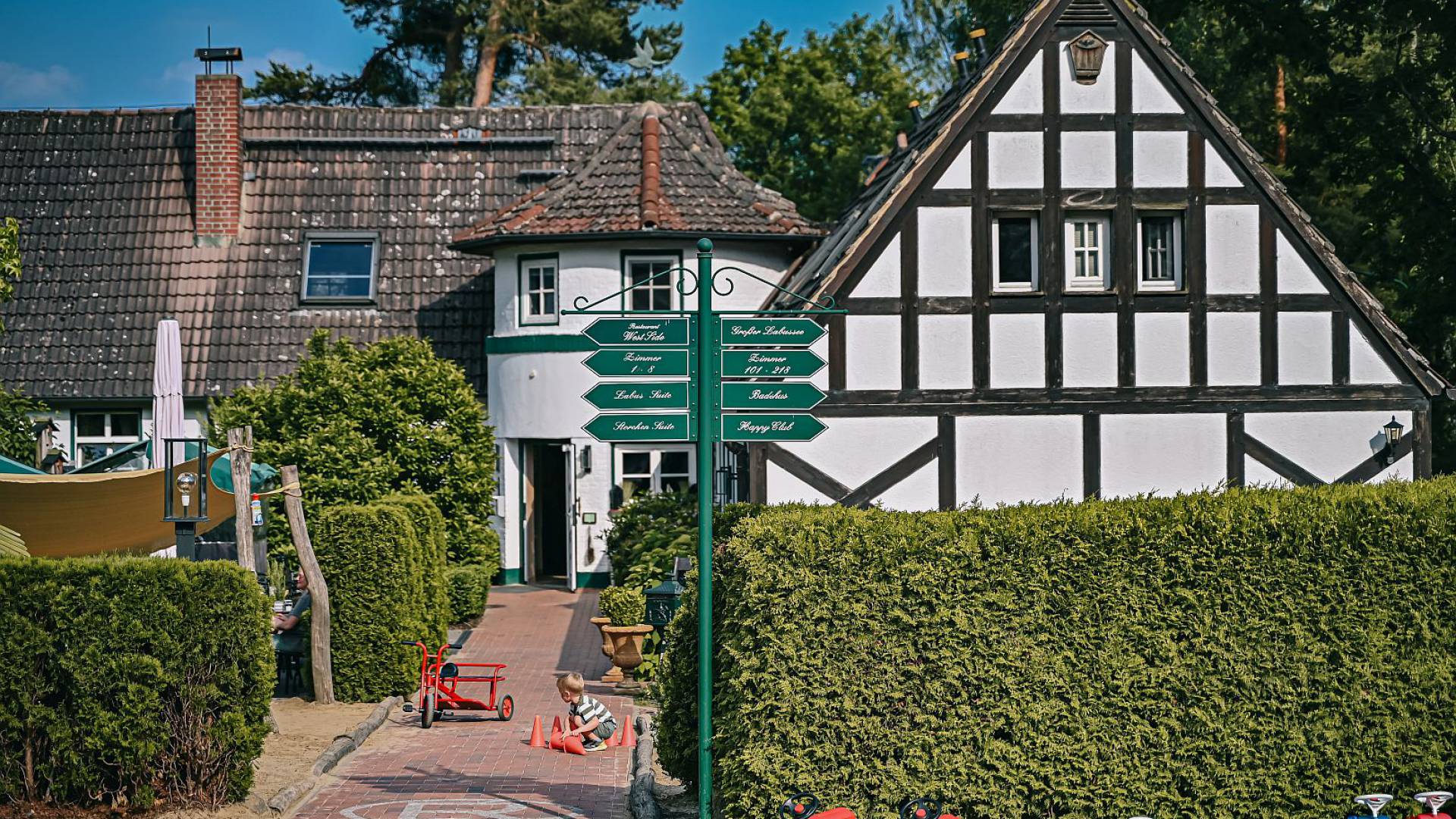 Haupthaus des Borchards Rookhus im Fachwerk Stil, mit Wegschildern und ein Kind spielt mit Hütchen am Boden