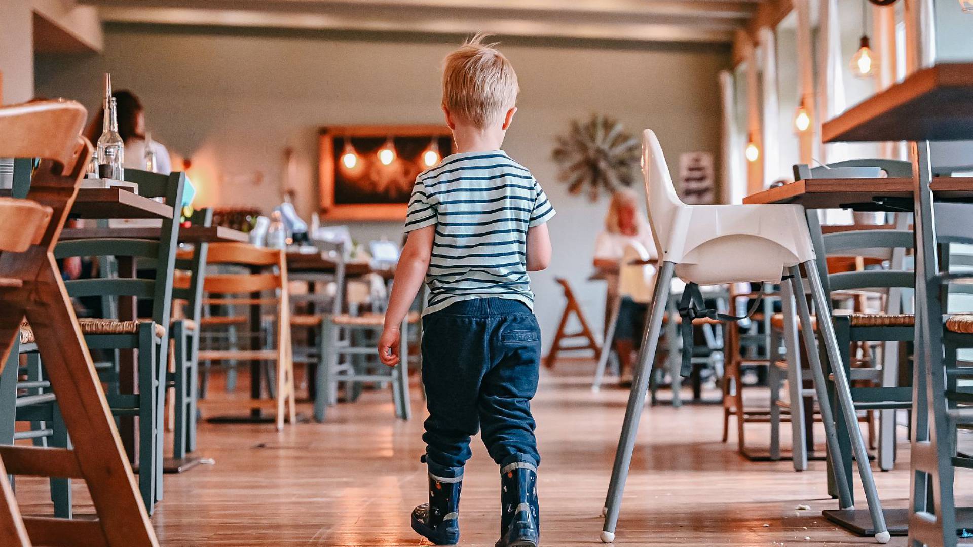 Kleiner Junge mit Gummistiefel läuft durch das Restaurant