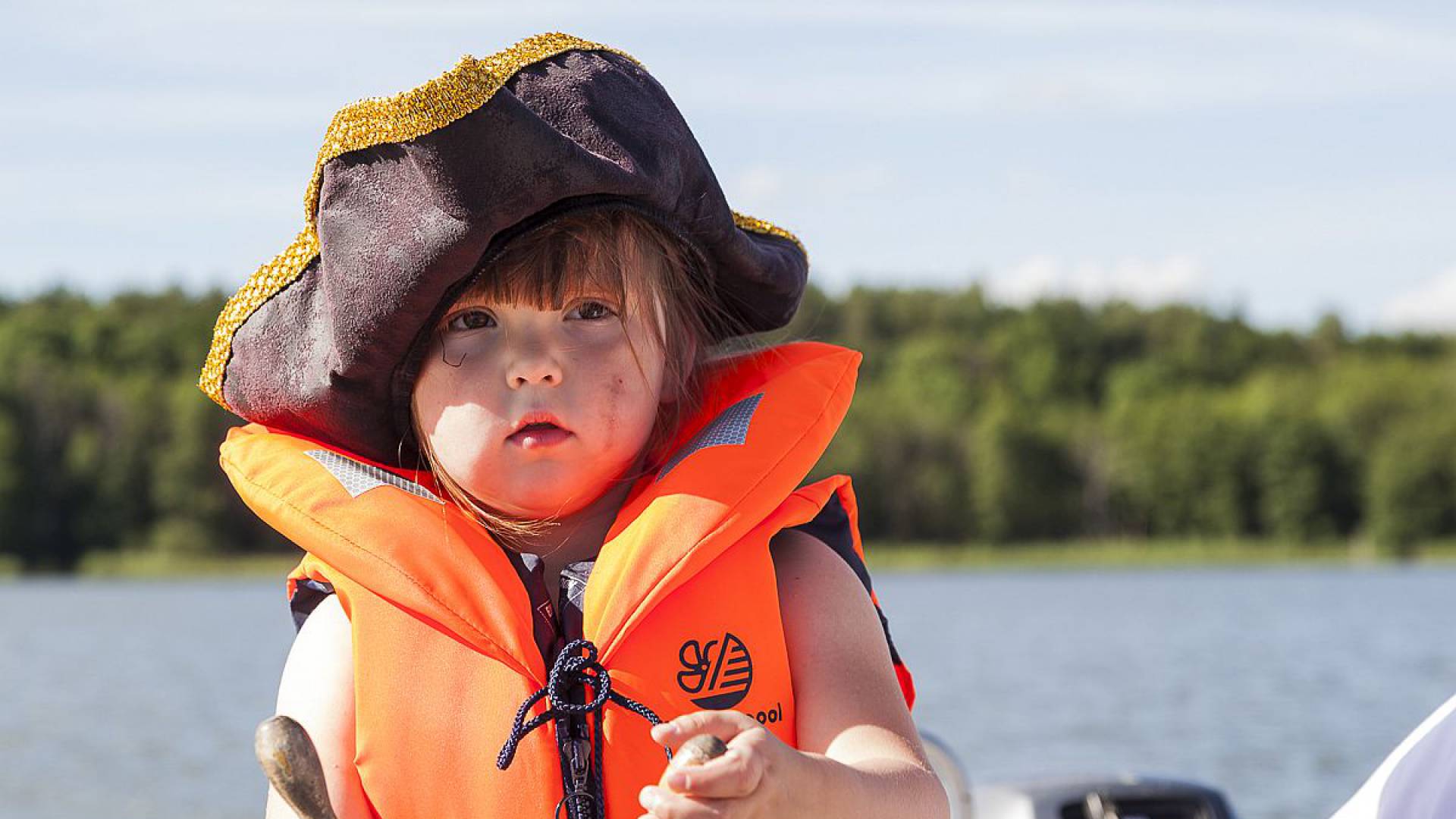 Kleiner Junge mit Schwimmweste, Piratenhut und Steuer in den Händen auf dem Labussee