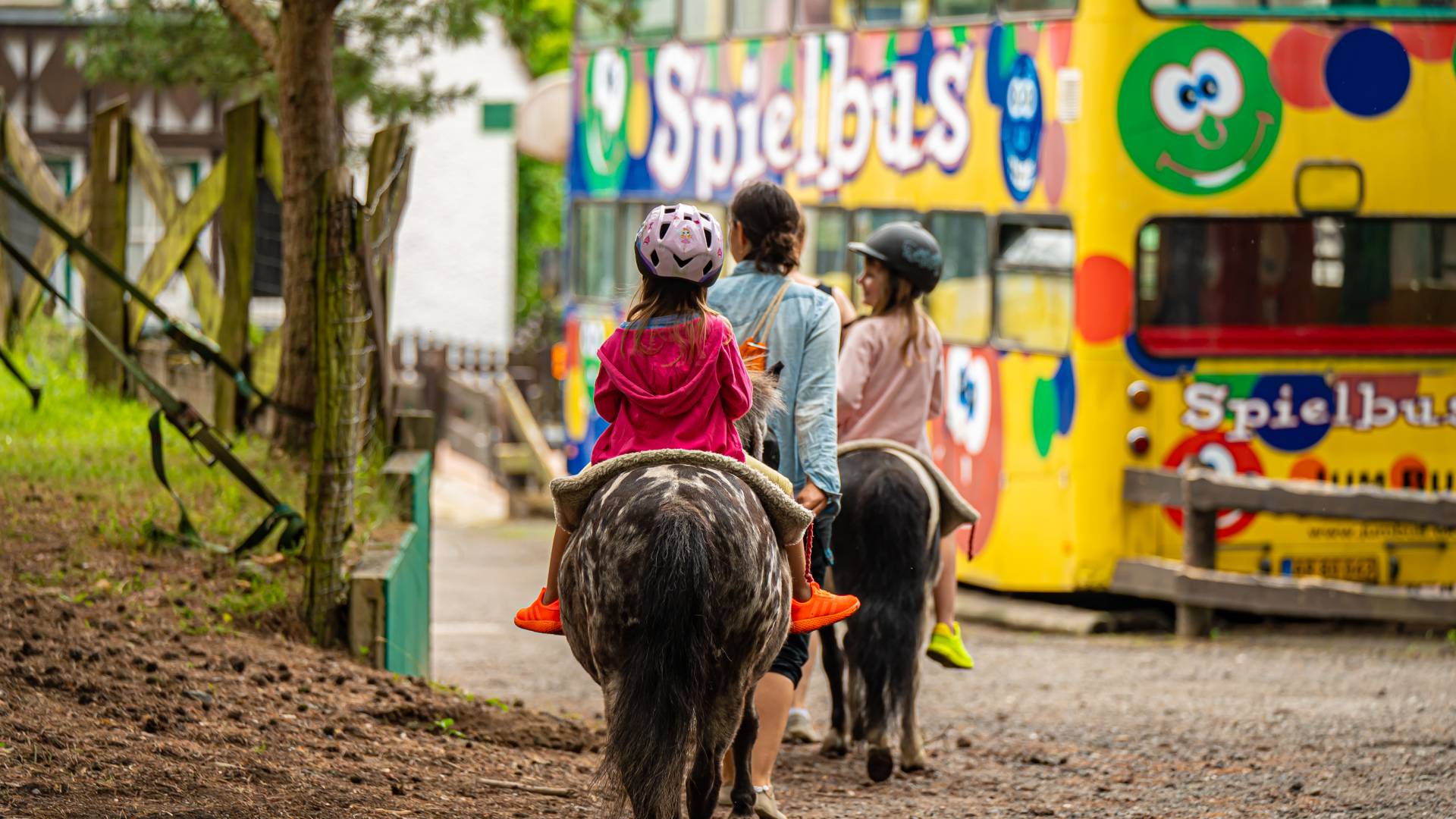 Kinder reiten auf Ponys im Hintergrund ist ein Spielbus zu sehen